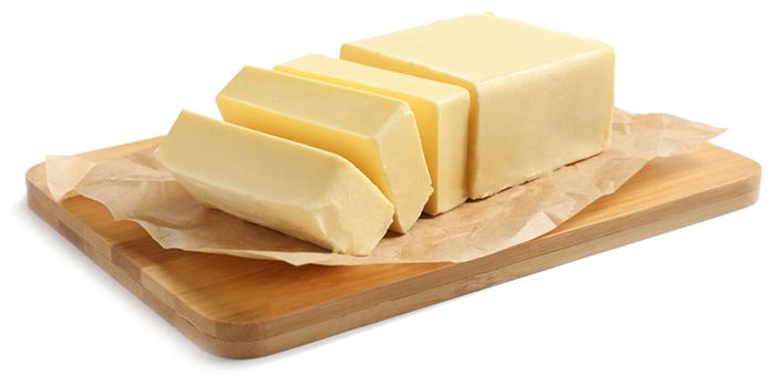 block of butter on a brown wooden board, 3 slices cut into the butter. On a white isolated background