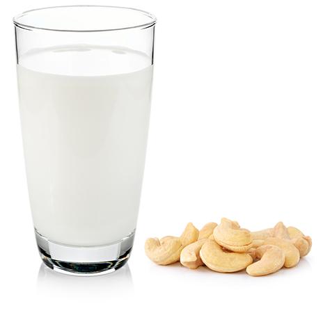 Glass of cashew nut milk surrounded my cashews, on isolated white background