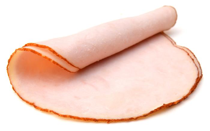 Rounded piece of slicked ham folding at one end, on a white isolated background