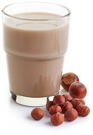 Isolated white background, a glass of hazelnut milk, surrounded by hazelnuts