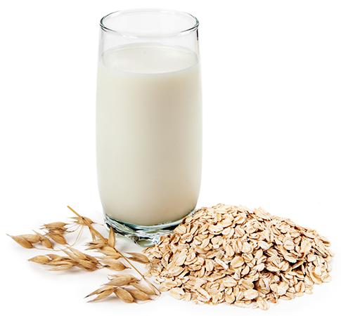 Glass of oat milk, with oats laying at the base of the glass on a silhouette white background